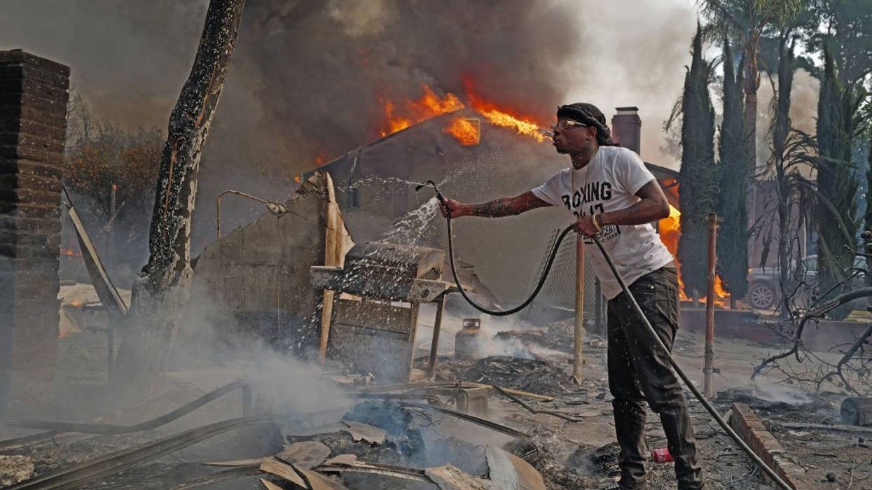 Man pours water from a hose on smoldering fire in Altadena