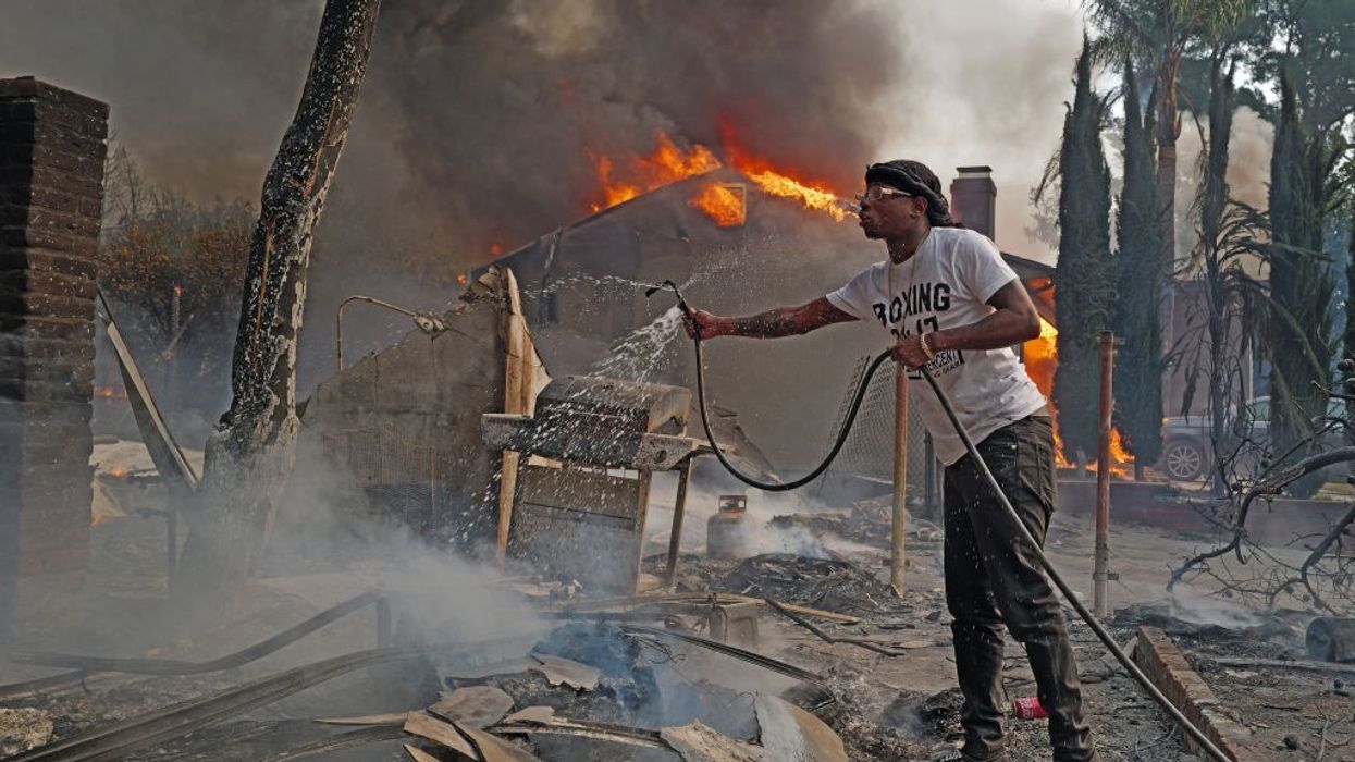 Man pours water from a hose on smoldering fire in Altadena