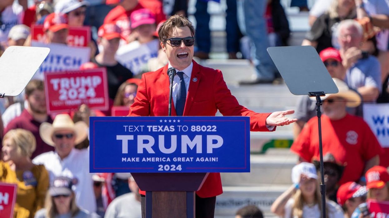 Matt Gaetz addresses a Trump rally wearing a red suit, white shirt, blue tie, and and sunglasses