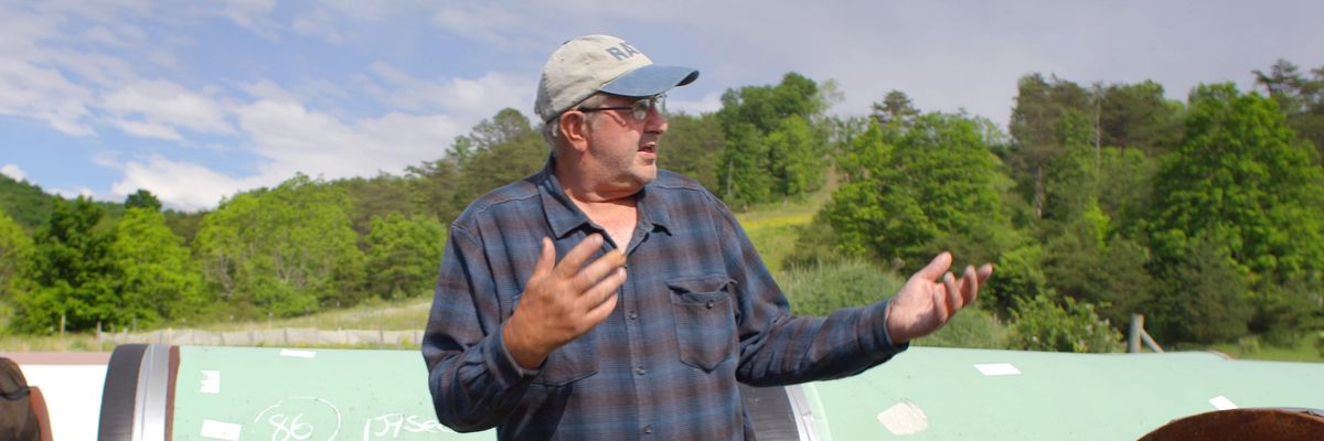 Maury Johnson standing near his West Virginia farm with pieces of pipeline in the background.