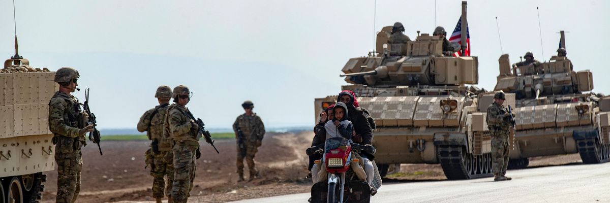 Members of a Syrian family ride a motorcycle as a U.S. military convoy patrols