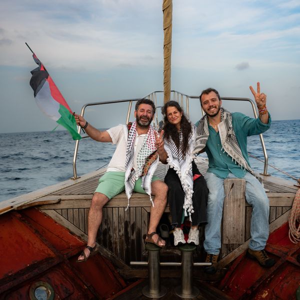 Members of the Global Sumud Flotilla wave a Palestinian flag and make a peace symbol with their hands.