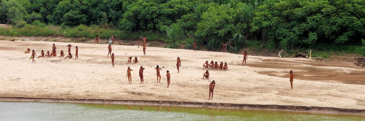 Members of the Mashco-Piro people stand and sit on a riverbank in the Peruvian Amazon