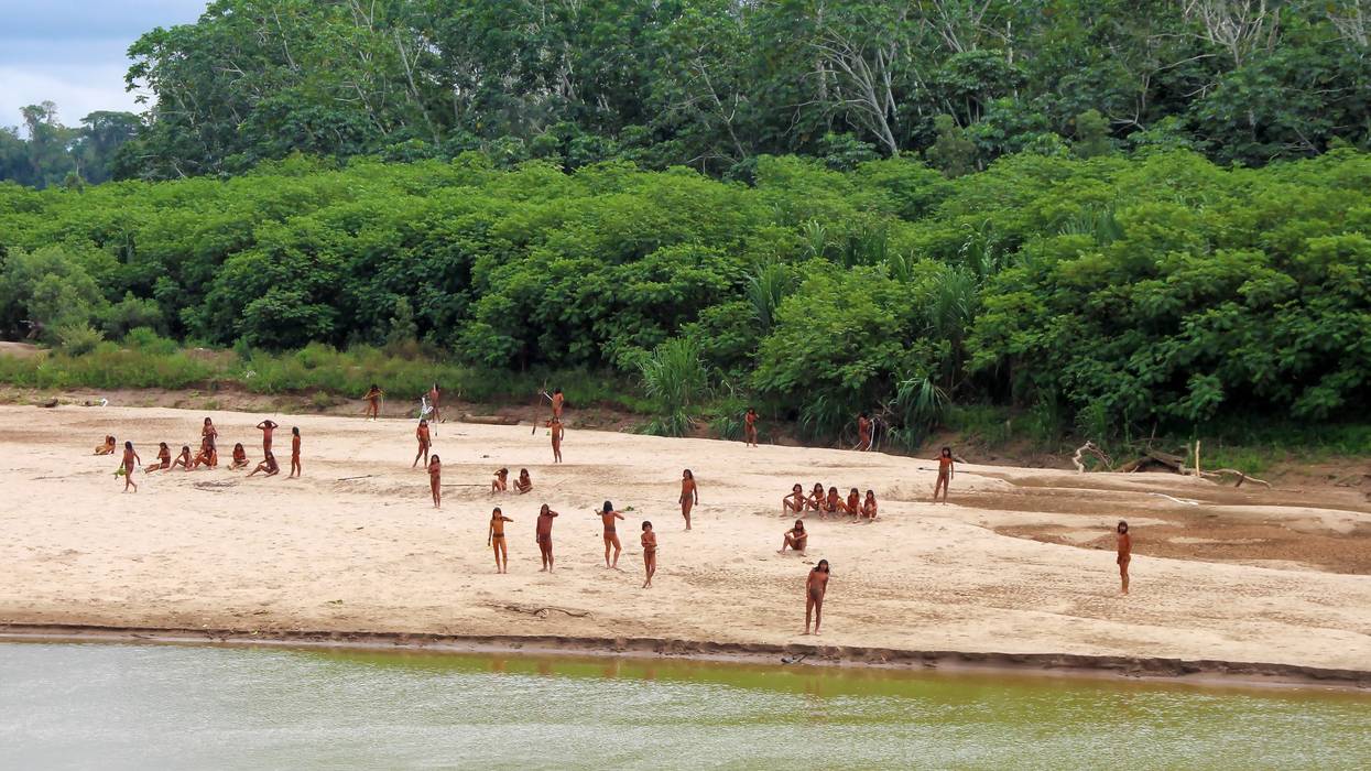 Members of the Mashco-Piro people stand and sit on a riverbank in the Peruvian Amazon