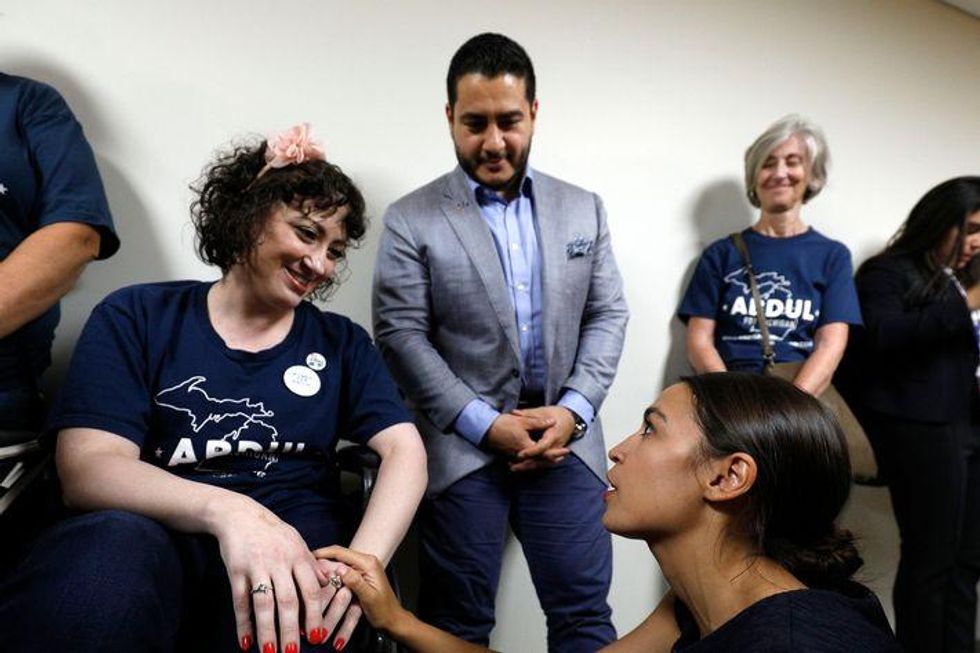 Michigan Democratic gubernatorial candidate Abdul El-Sayed (background) and New York Democrat candidate for Congress Alexandria Ocasio-Cortez (sitting, right) speak with a supporter in a wheel chair after the two campaigned together at a rally on the campus of Wayne State University July 28, 2018 in Detroit, Michigan.