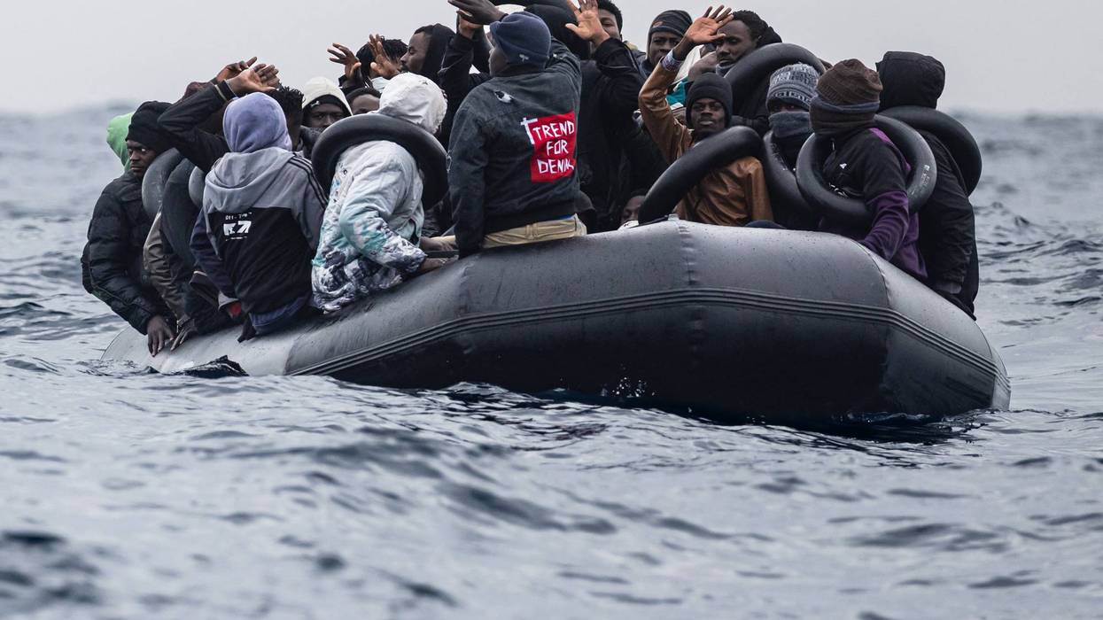 Migrants onboard a rubber boat wave and gesture as they wait to be rescued