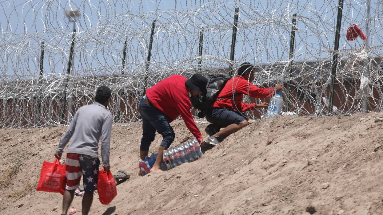 Migrants outside razor wire at US-Mexican border.