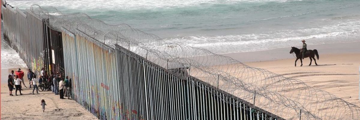 migrants stand on a beach beside the U.S.-Mexico border wall