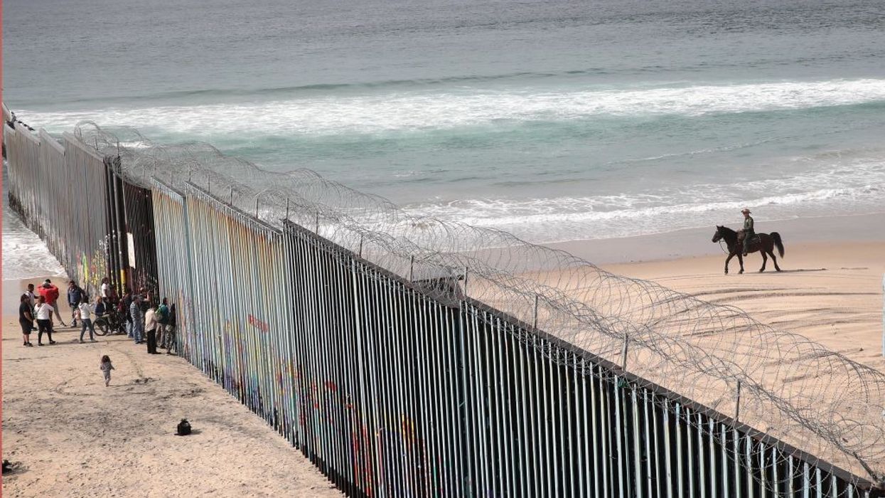 migrants stand on a beach beside the U.S.-Mexico border wall