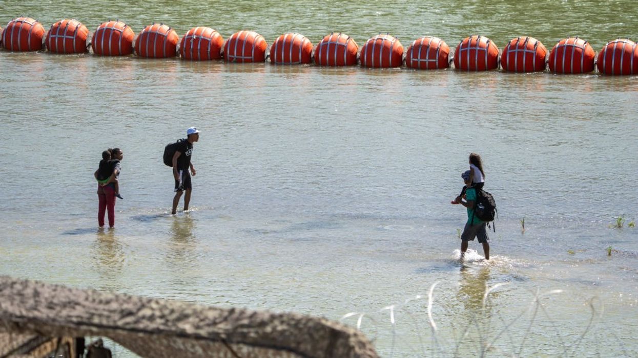 Migrants walk by a floating barrier along the Rio Grande