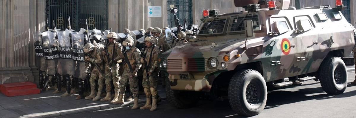 Military members stand guard with an armored truck