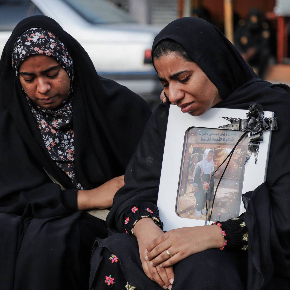 Mourning Iranian women hold a photo of a girl killed in the US strike on a school in Minab
