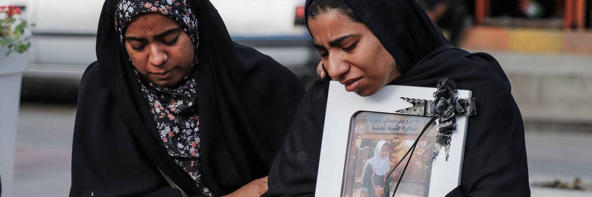 Mourning Iranian women hold a photo of a girl killed in the US strike on a school in Minab