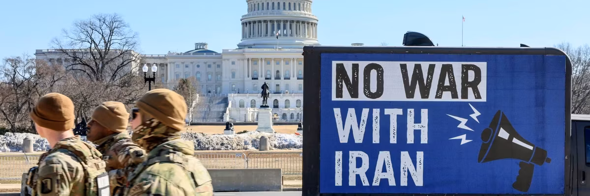 National Guardsman walk past Capitol building and "No War With Iran" billboard truck.