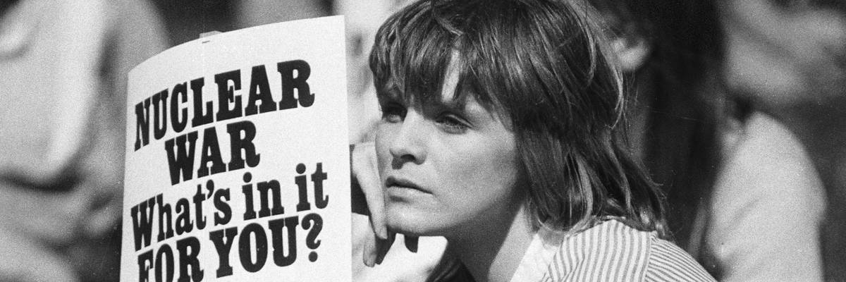 Nuclear war opponent holds sign that says "Nuclear War: What is in it for you?"