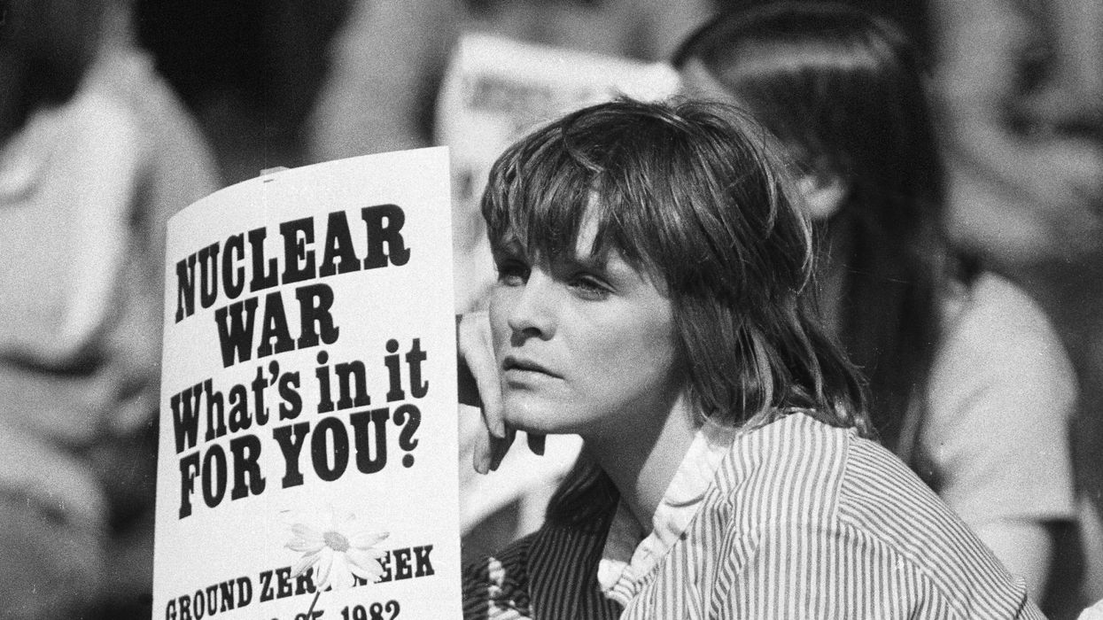 Nuclear war opponent holds sign that says "Nuclear War: What is in it for you?"