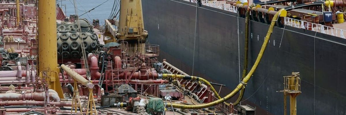 Oil is transferred from one tanker to another via yellow tubes.