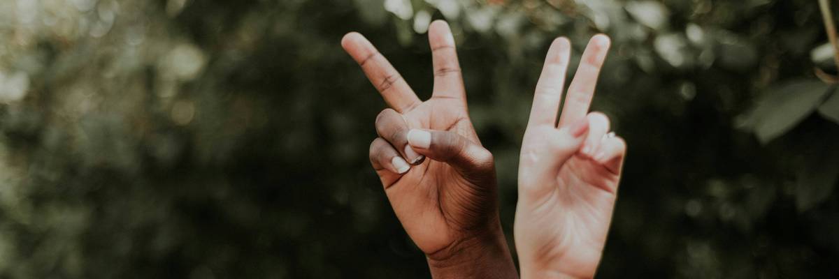 One dark- and one light-skinned hand make peace signs.