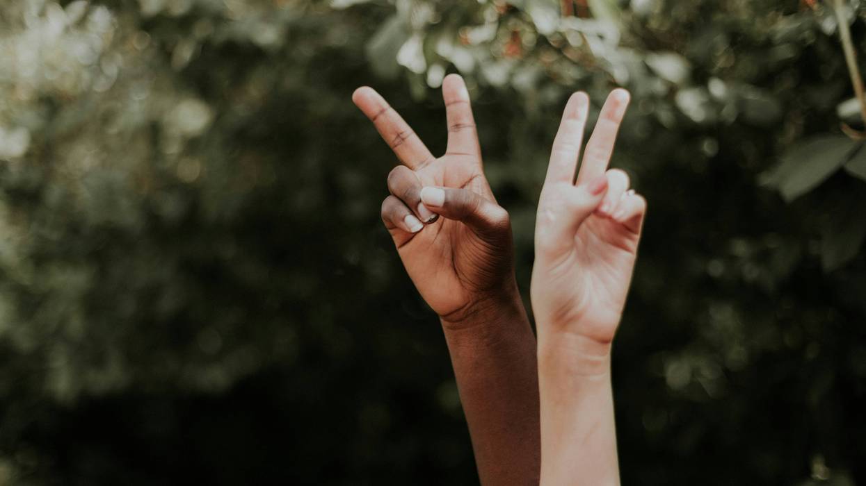 One dark- and one light-skinned hand make peace signs.