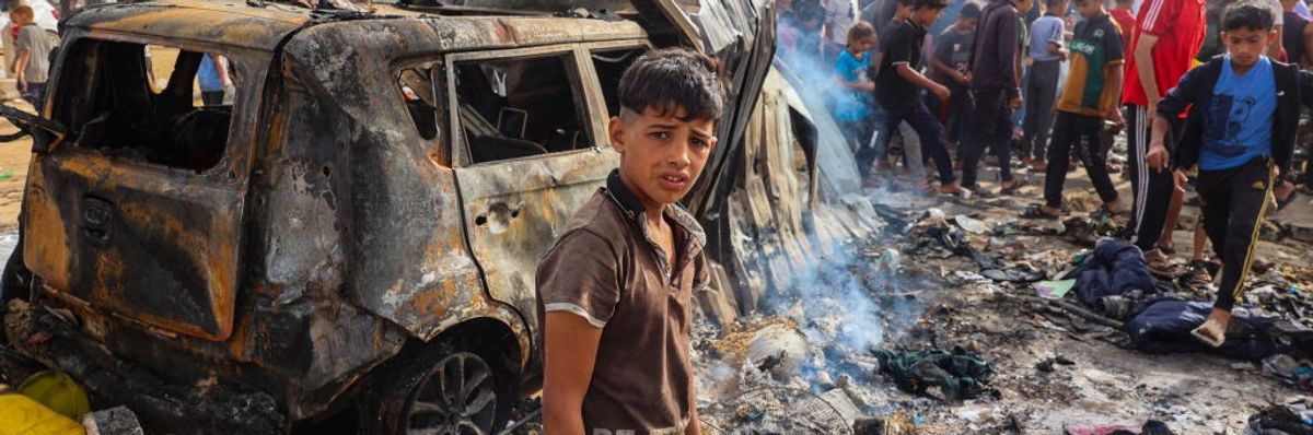 Palestinian boy standing in front of burned car