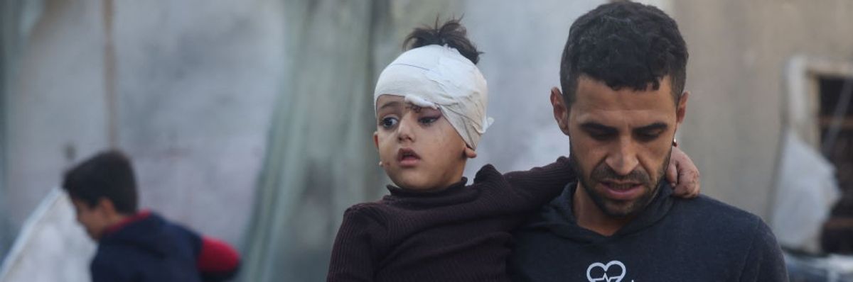 Palestinian boy with bandaged head held by a man in Gaza