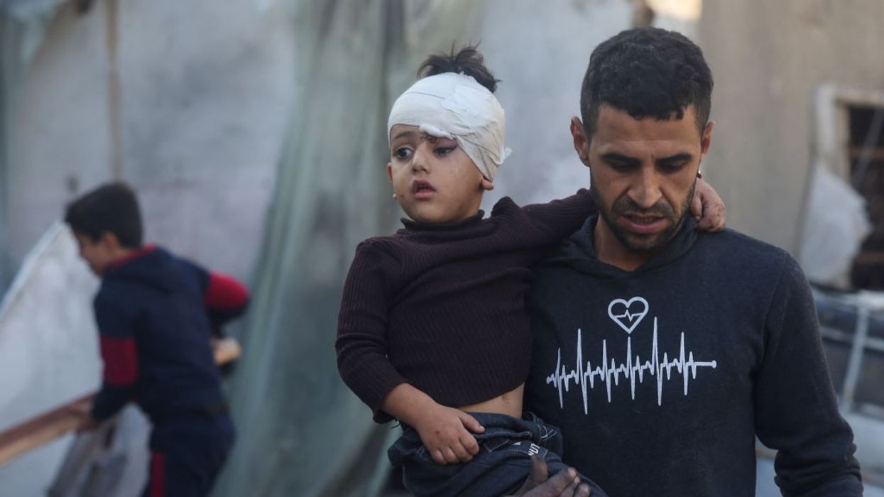 Palestinian boy with bandaged head held by a man in Gaza