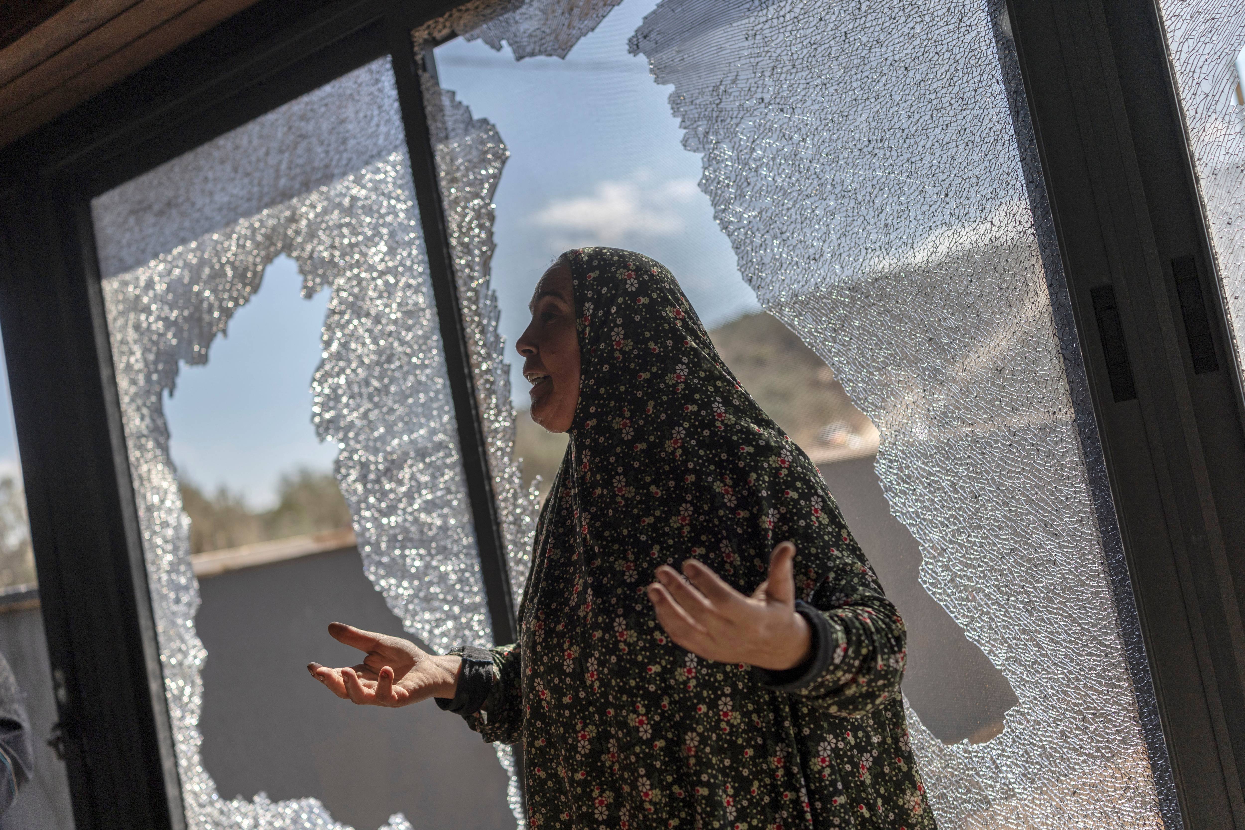 Palestinian Hanan Hamayei gestures as she stands near the shattered glass of her home following a reported attack by Israeli settlers, in the Israeli-occupied West Bank village of Turmus 'Ayya, on October 19, 2026.