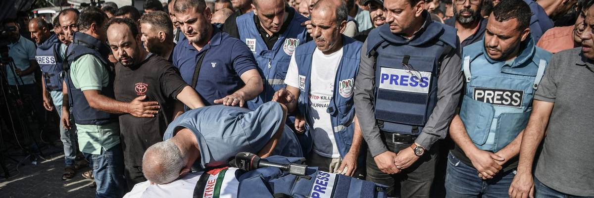 Palestinian journalists in blue "PRESS" flak vests mourn the killing of a colleague by Israeli forces.