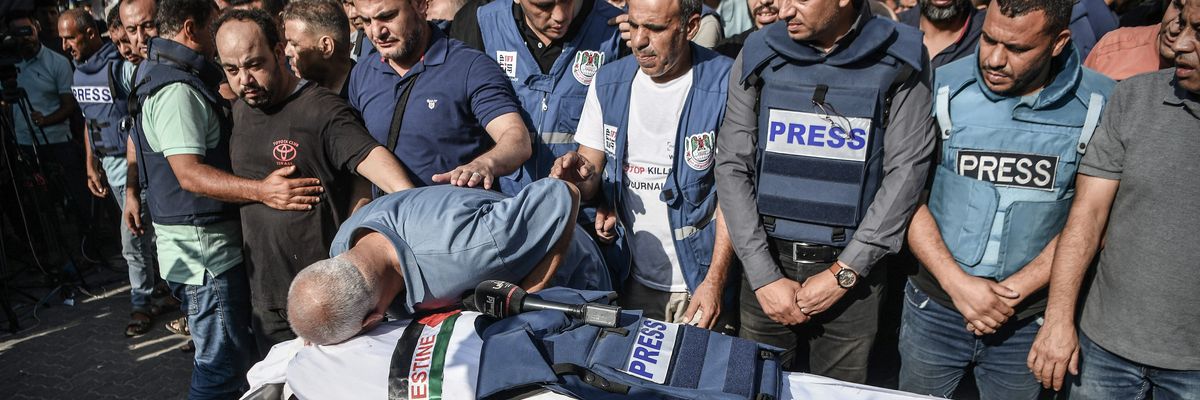 Palestinian journalists in blue "PRESS" flak vests mourn the killing of a colleague by Israeli forces.