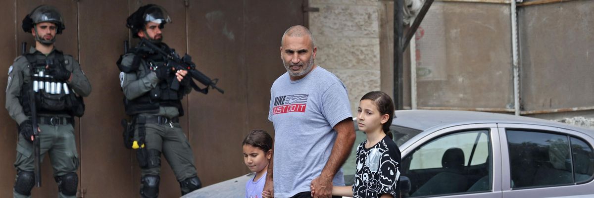 Palestinian man walking with his children with Israeli soldiers in the background