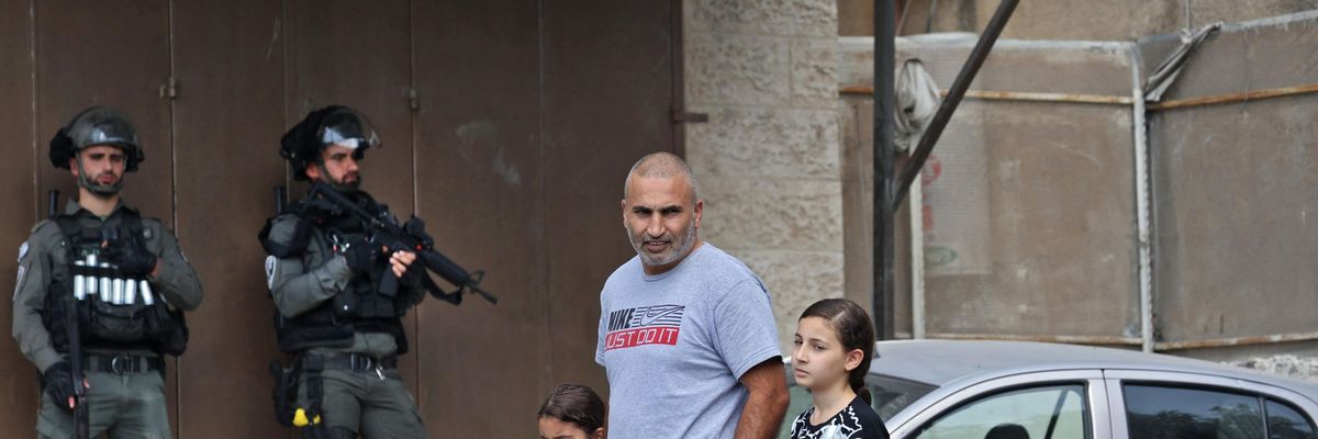 Palestinian man walking with his children with Israeli soldiers in the background