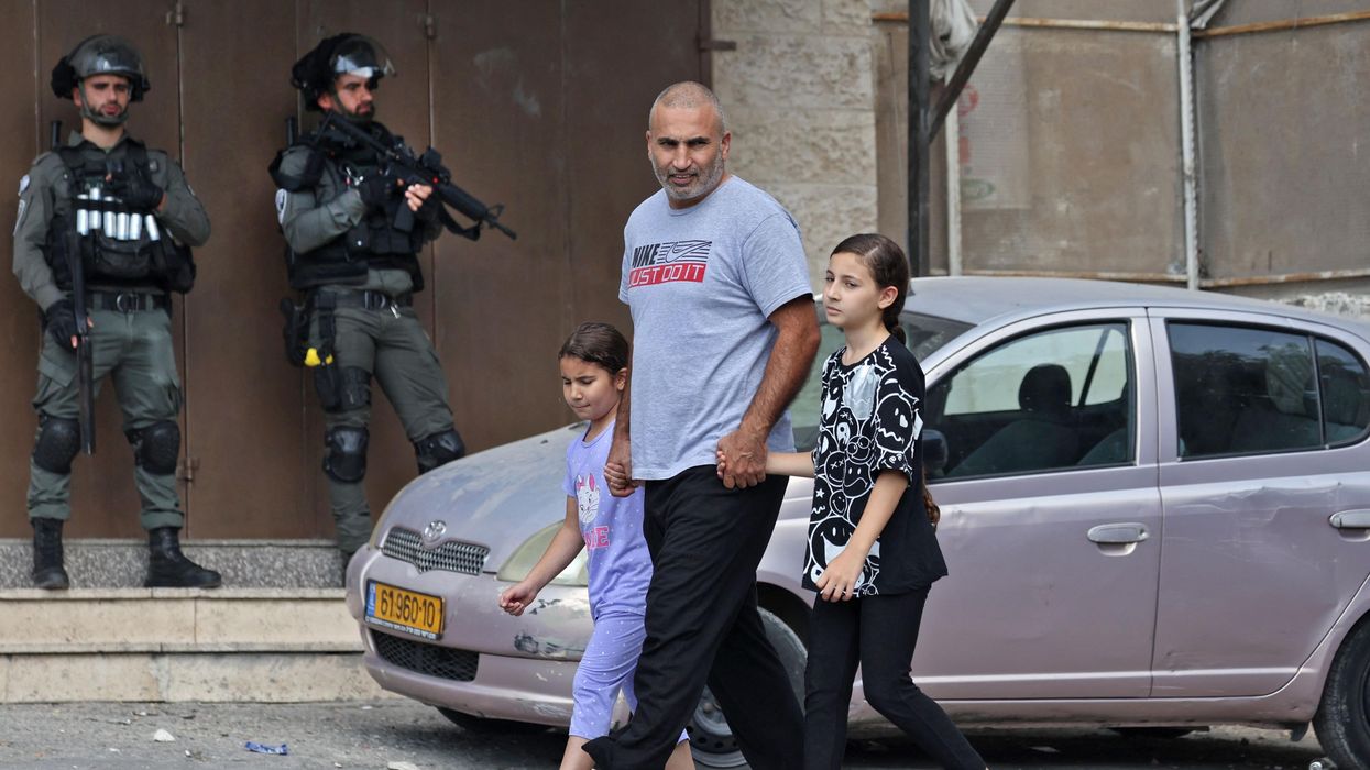 Palestinian man walking with his children with Israeli soldiers in the background
