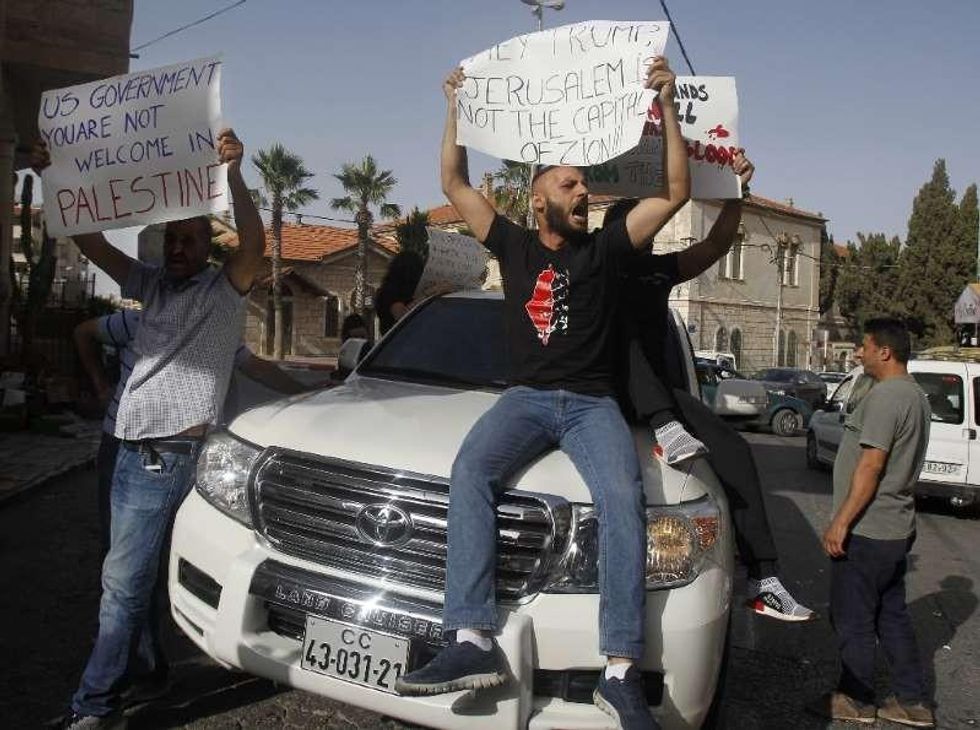 Palestinian men holding signs with anti-US slogans sit atop a car carrying members of a US delegation to protest their visit to the occupied West Bank on May 22, 2018. (Photo: AFP)