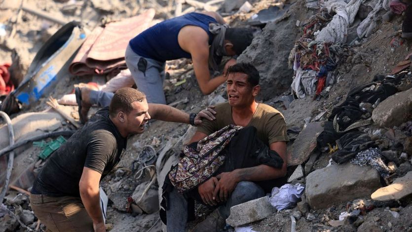 Palestinian men mourn on a pile of rubble after Israeli airstrike