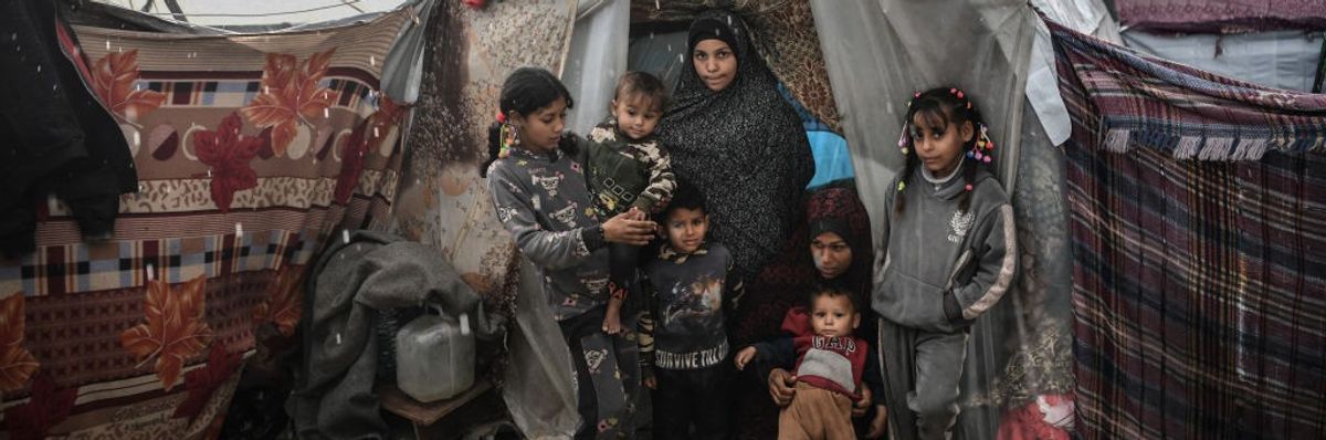 Palestinian women and children under a plastic tent as refugees in Rafah
