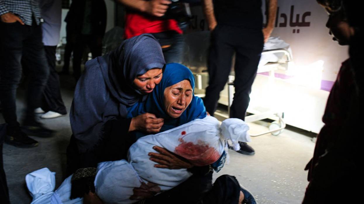 Palestinian women weep as one holds the shrouded body of a child killed by an Israeli strike