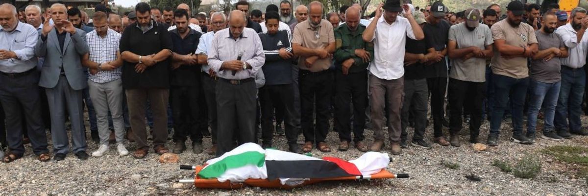 Palestinians pray over the the body of Hanan Abu Salameh, which is lying on the ground shrouded in a Palestinian flag
