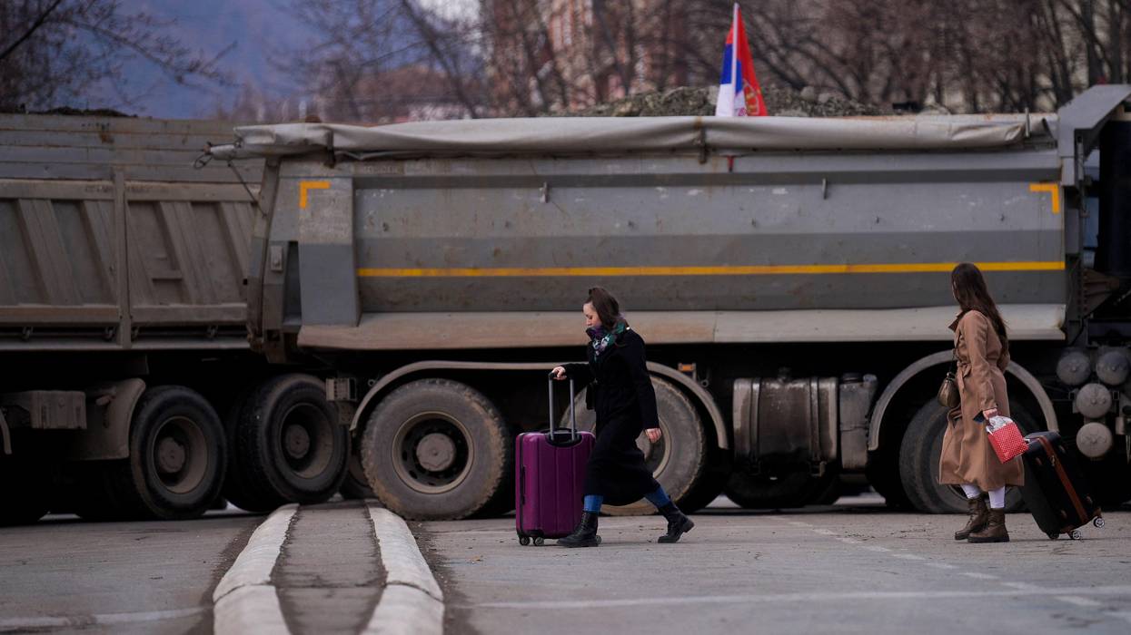 Pedestrians walk past a new road barricade set up in the divided town of Mitrovica, Kosovo on December 28, 2022.