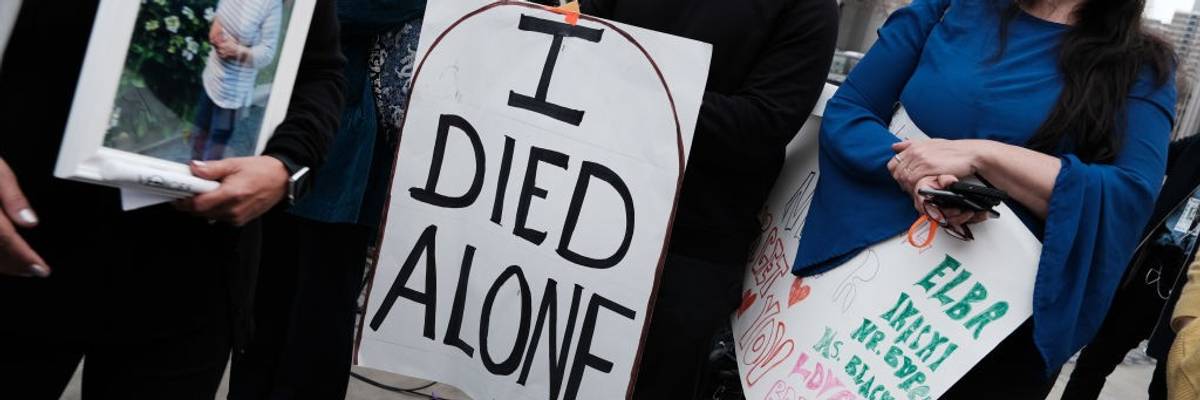 People attend a protest with the central figure holding a sign reading, "I died alone."