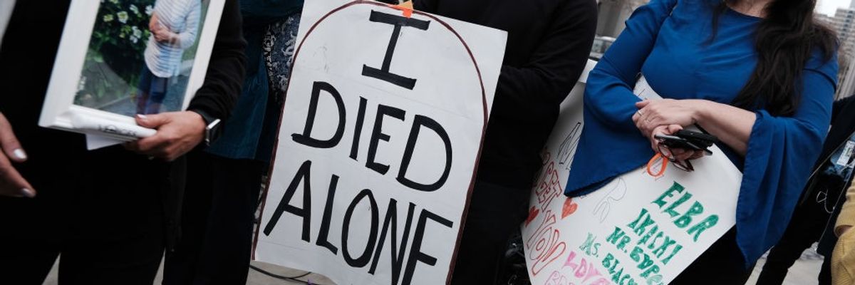 People attend a protest with the central figure holding a sign reading, "I died alone."
