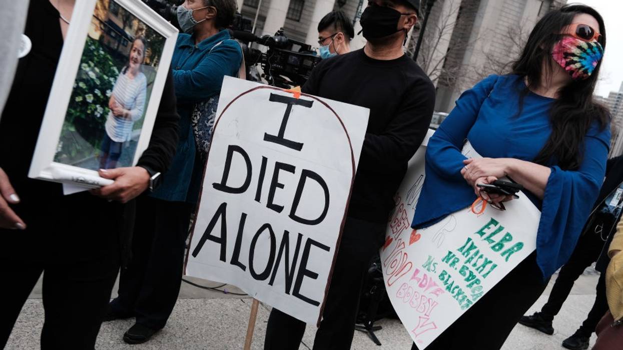People attend a protest with the central figure holding a sign reading, "I died alone."