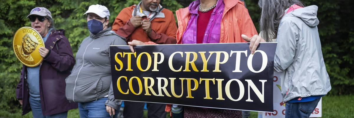 People hold a sign reading "Stop Crypto Corruption"