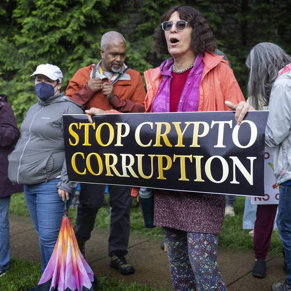 People hold a sign reading "Stop Crypto Corruption"