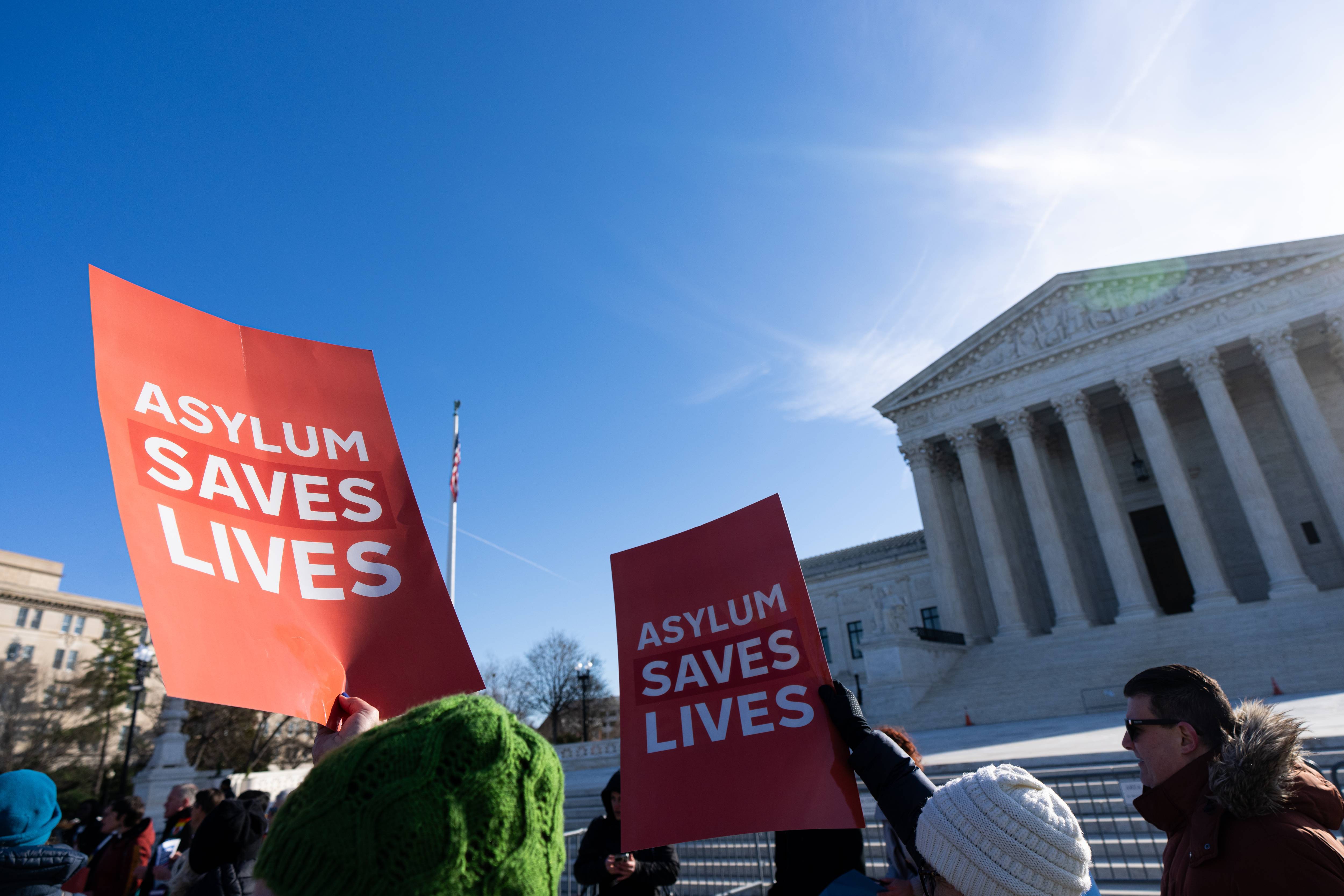 People hold "Asylum Saves Lives" posters outside the Supreme Court.