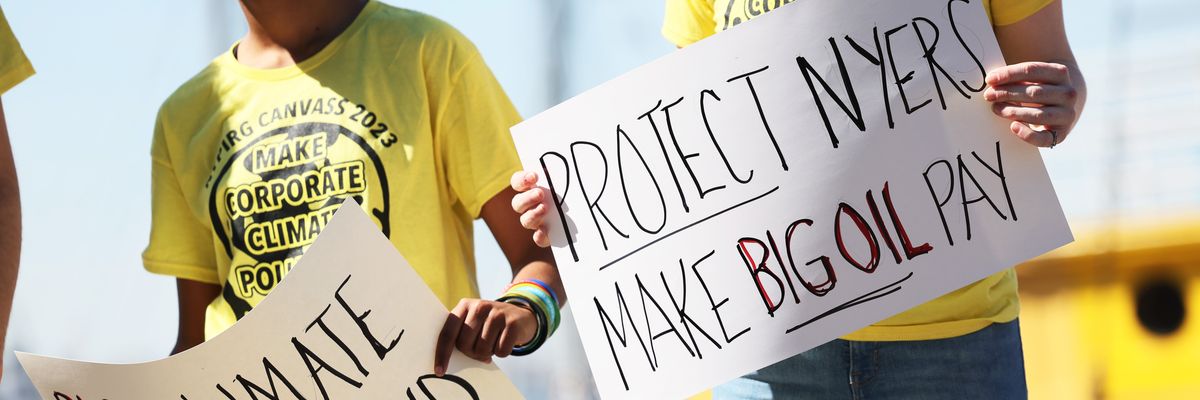 People hold signs during a press conference on the Climate Change Superfund Act