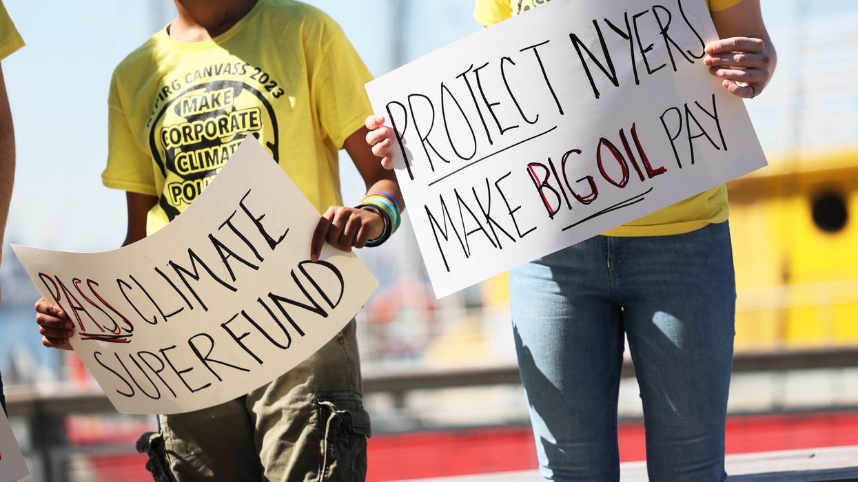 People hold signs during a press conference on the Climate Change Superfund Act
