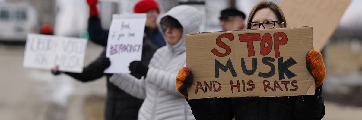 People hold signs during a protest against Elon Musk