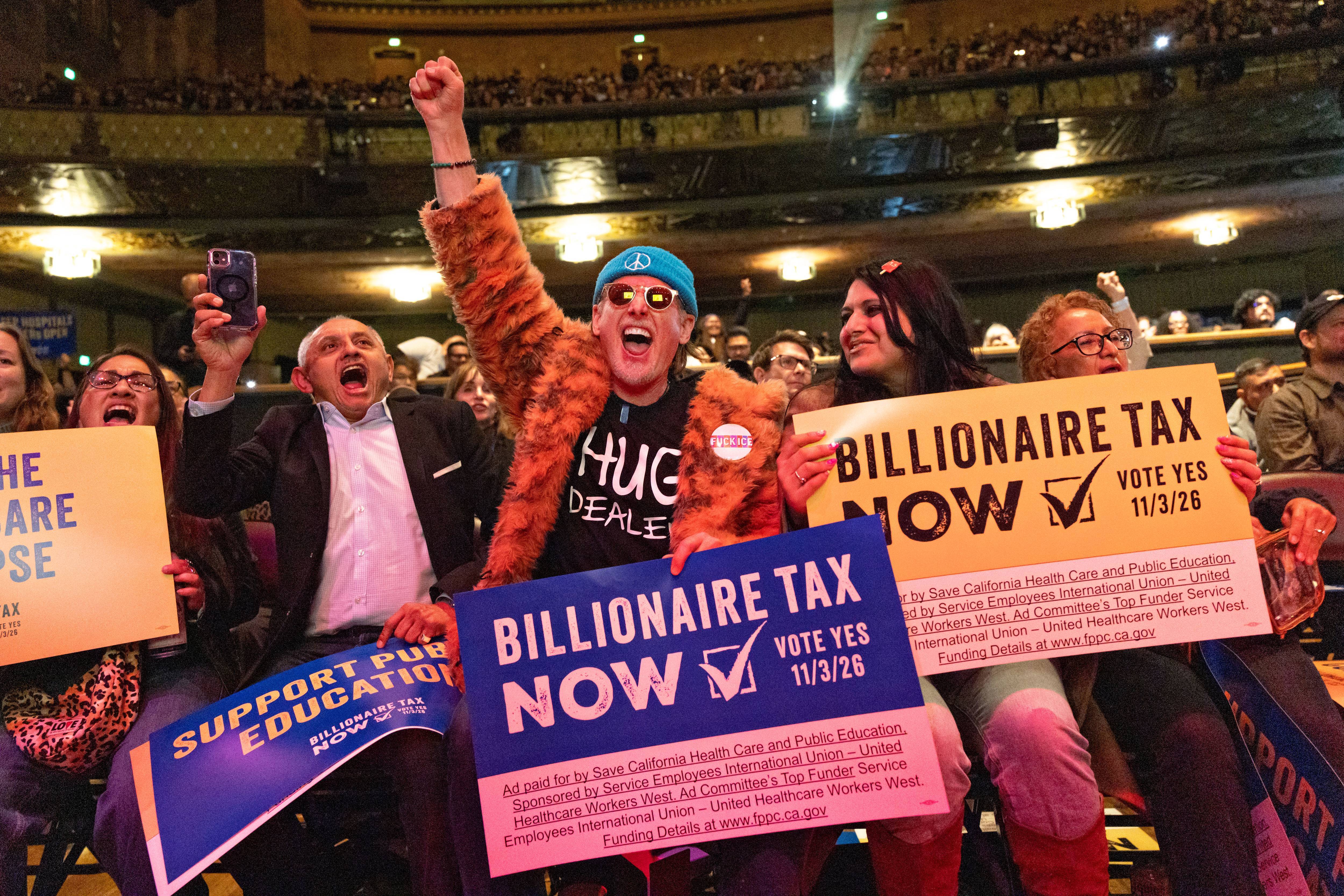 People hold signs reading, "Billionaire Tax Now" during a rally in Los Angeles