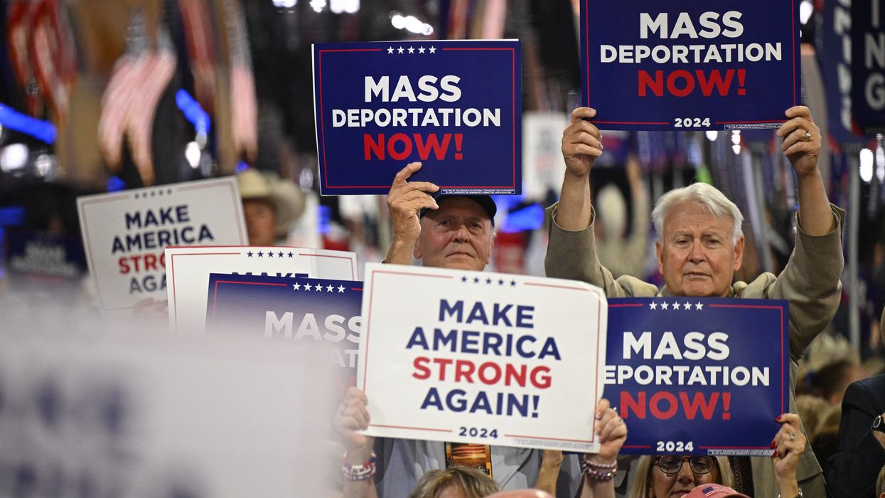 People hold signs reading, "Mass deportations now," at RNC.