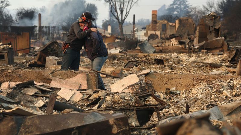 People hug in ruins of home destroyed in LA fires.